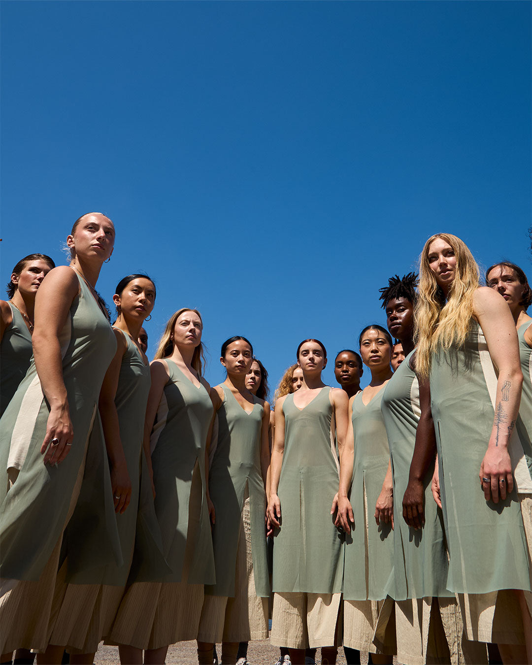 Group of women in matching dresses standing against a clear blue sky.
