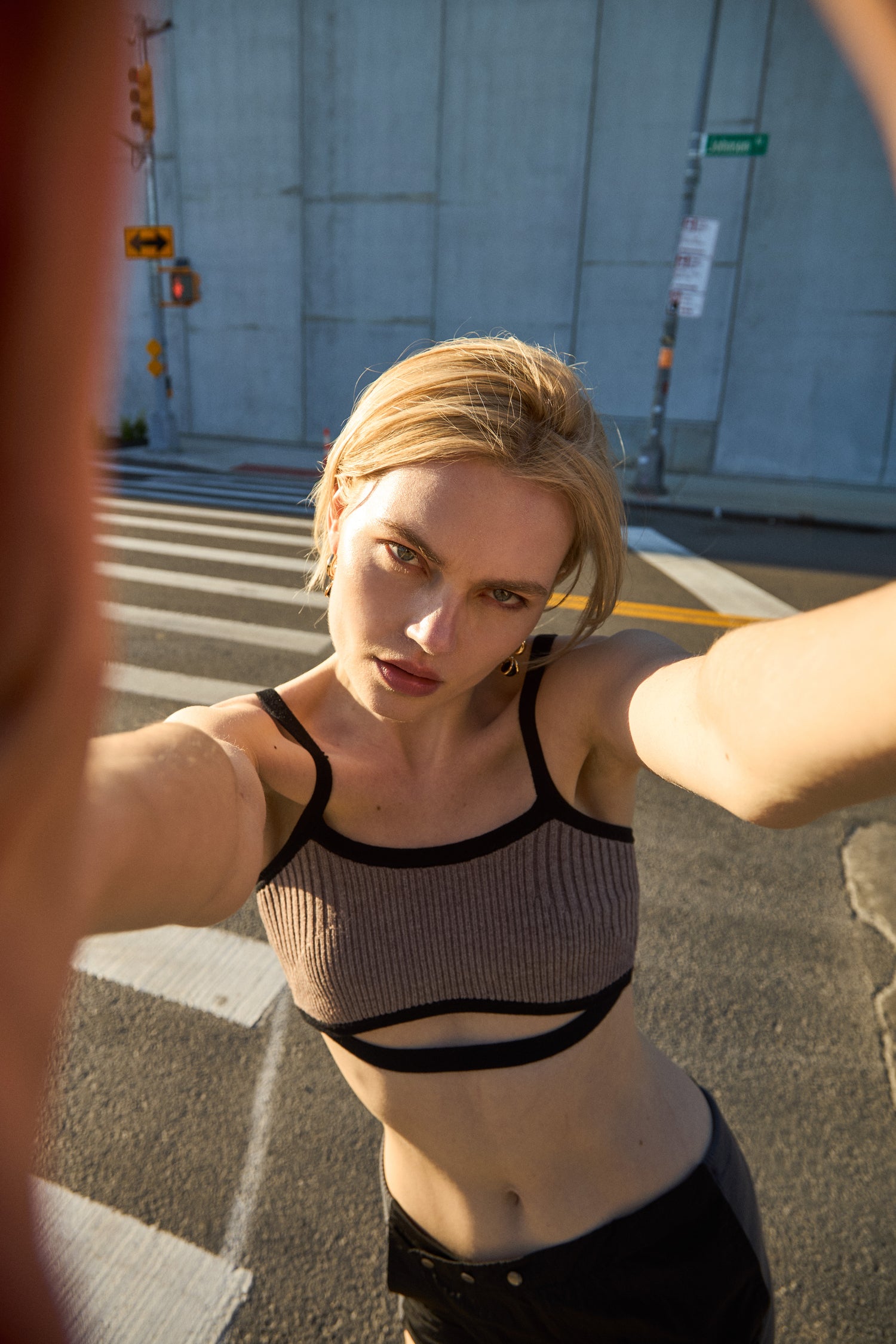 Model wearing 12Twelve Frame Knit in Sienna Clay, styled with black track pants on city street in golden hour light