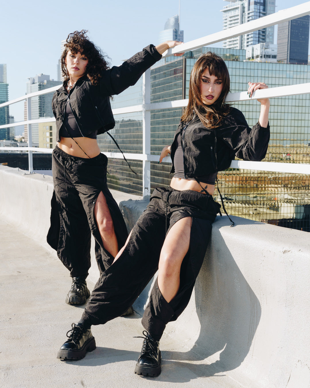 Two women in the 12Twelve Off-Duty Set posing on a rooftop, showing the lightweight black Track Pants with exaggerated slits and matching Crop Jackets.
