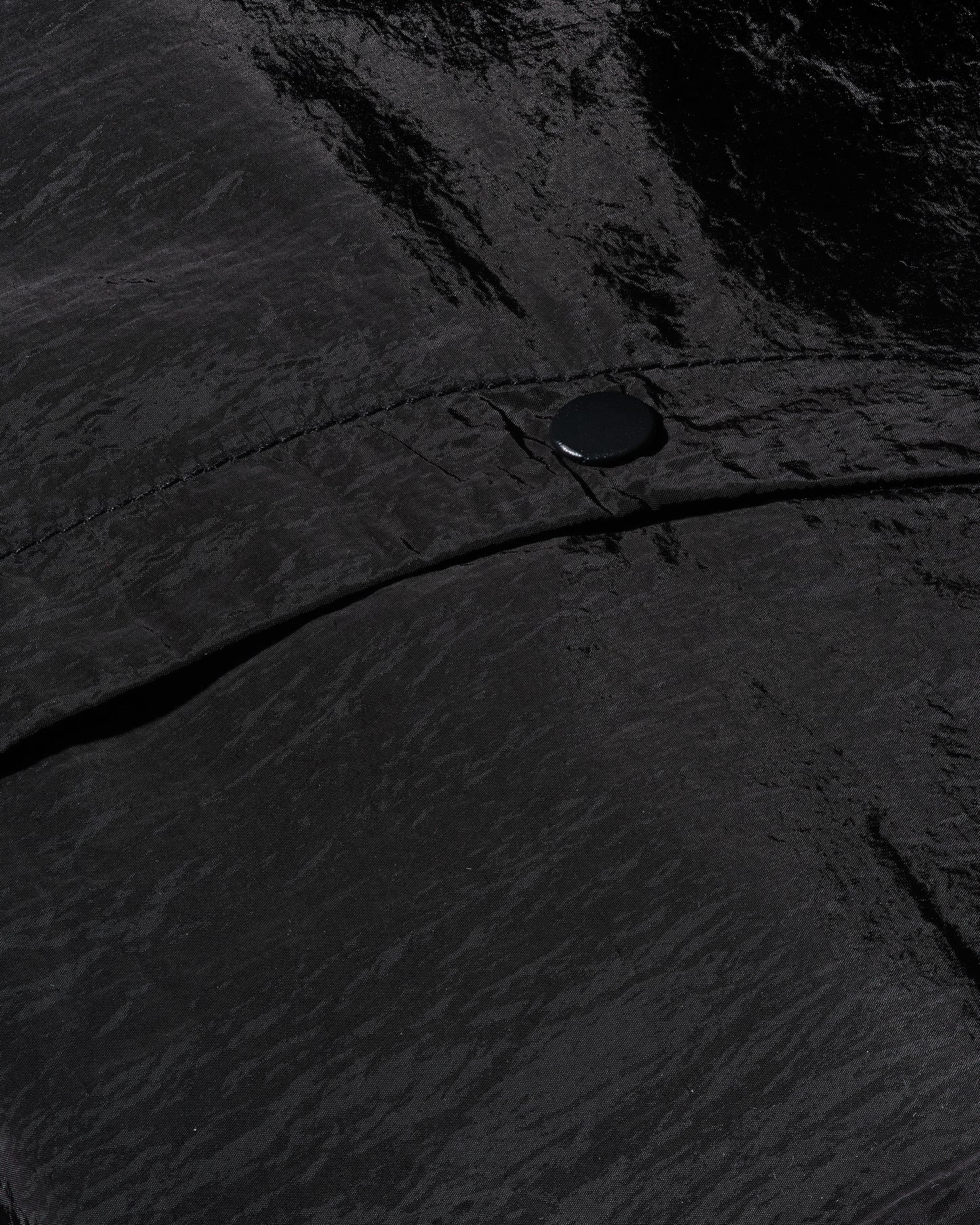 Detailed shot of 12Twelve track pants snap button and tonal seam on tech-style crinkle fabric