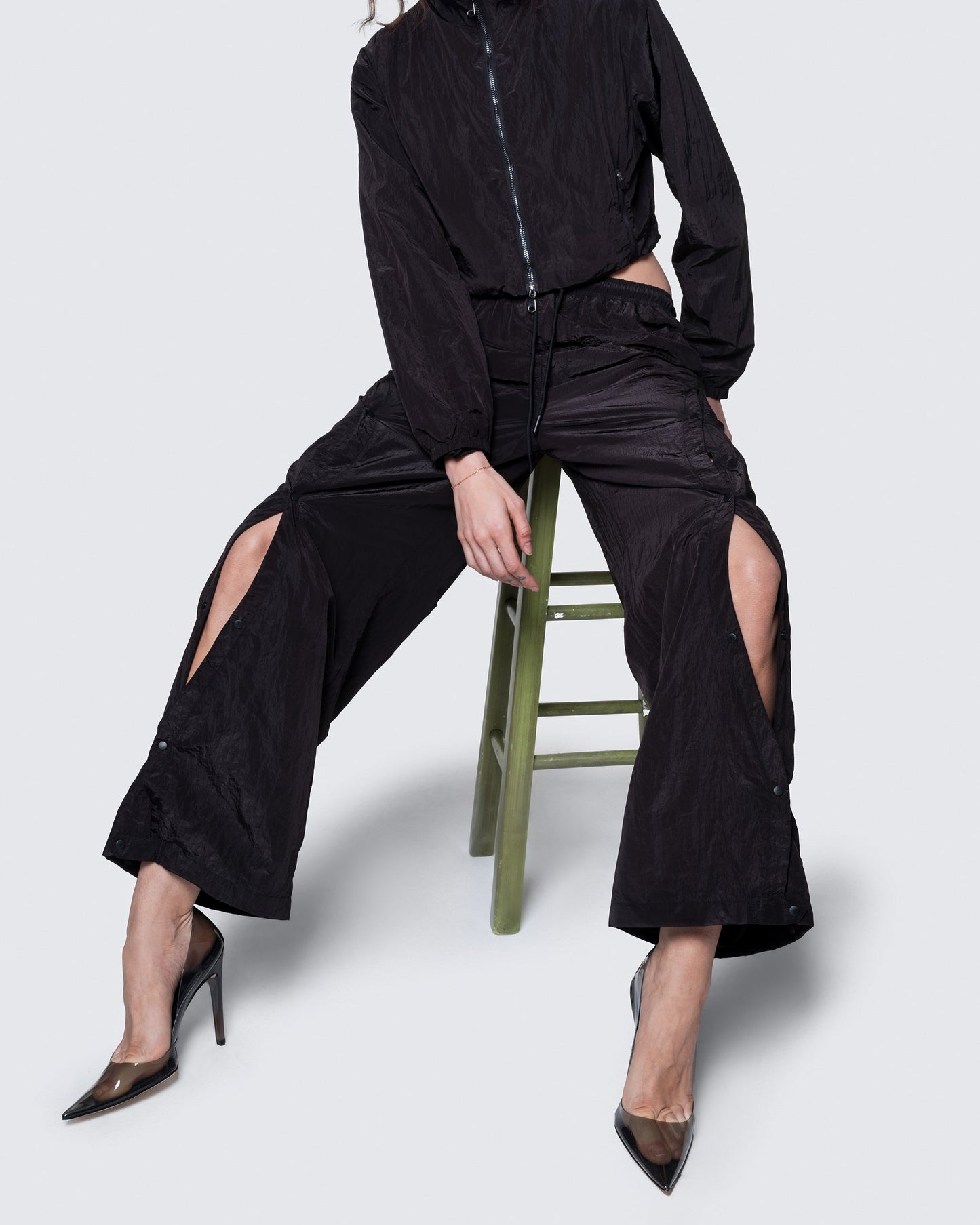 12Twelve black track pants styled with crop jacket, shown on model seated in studio setup