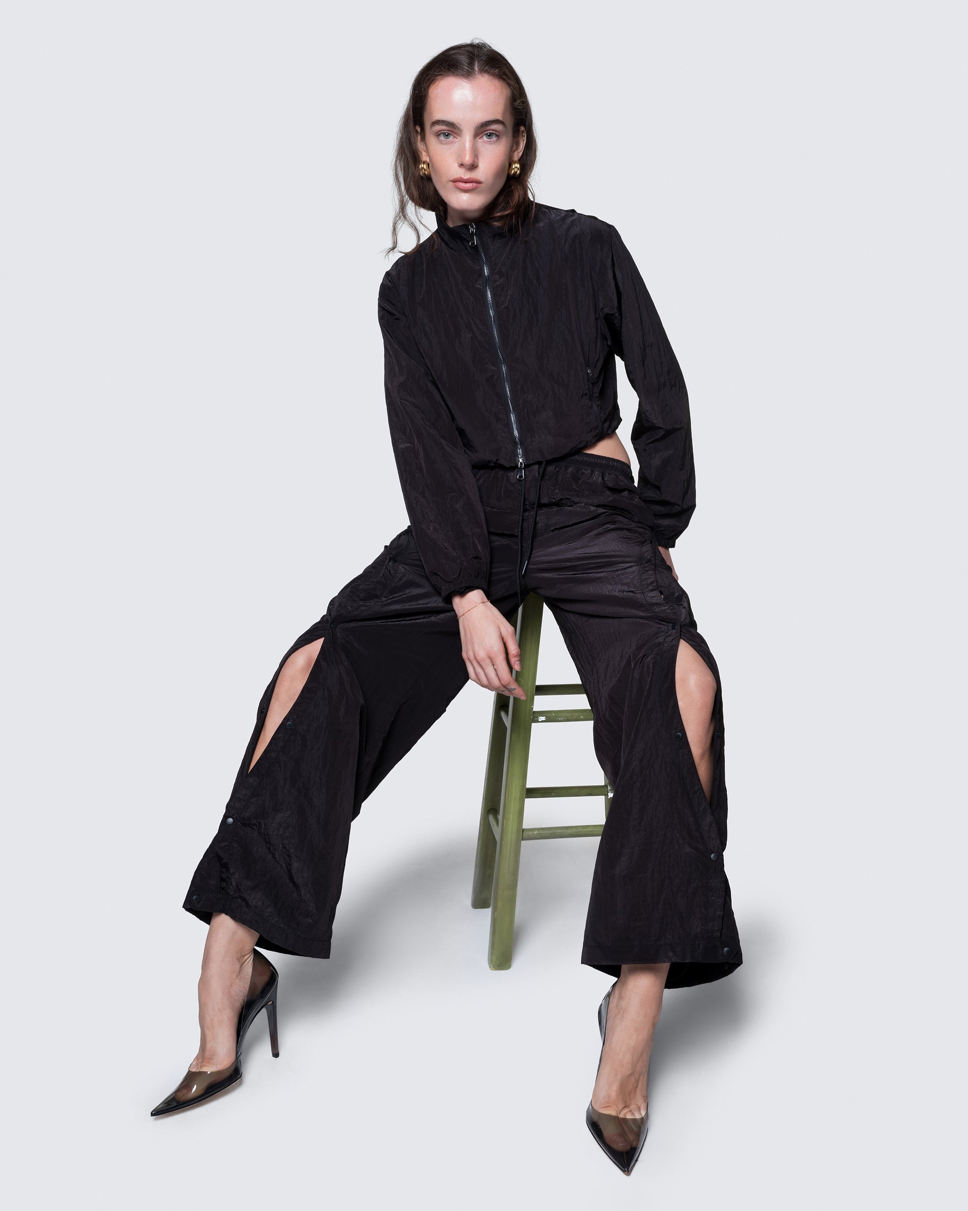 12Twelve black track pants styled with crop jacket, shown on model seated in studio setup