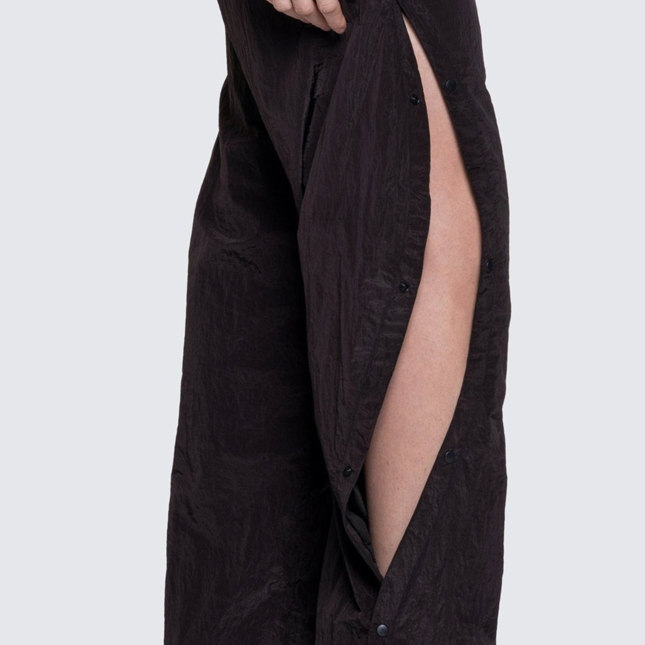 Side view of model in black 12twelve track pants showing the curved seam with tear away snaps.