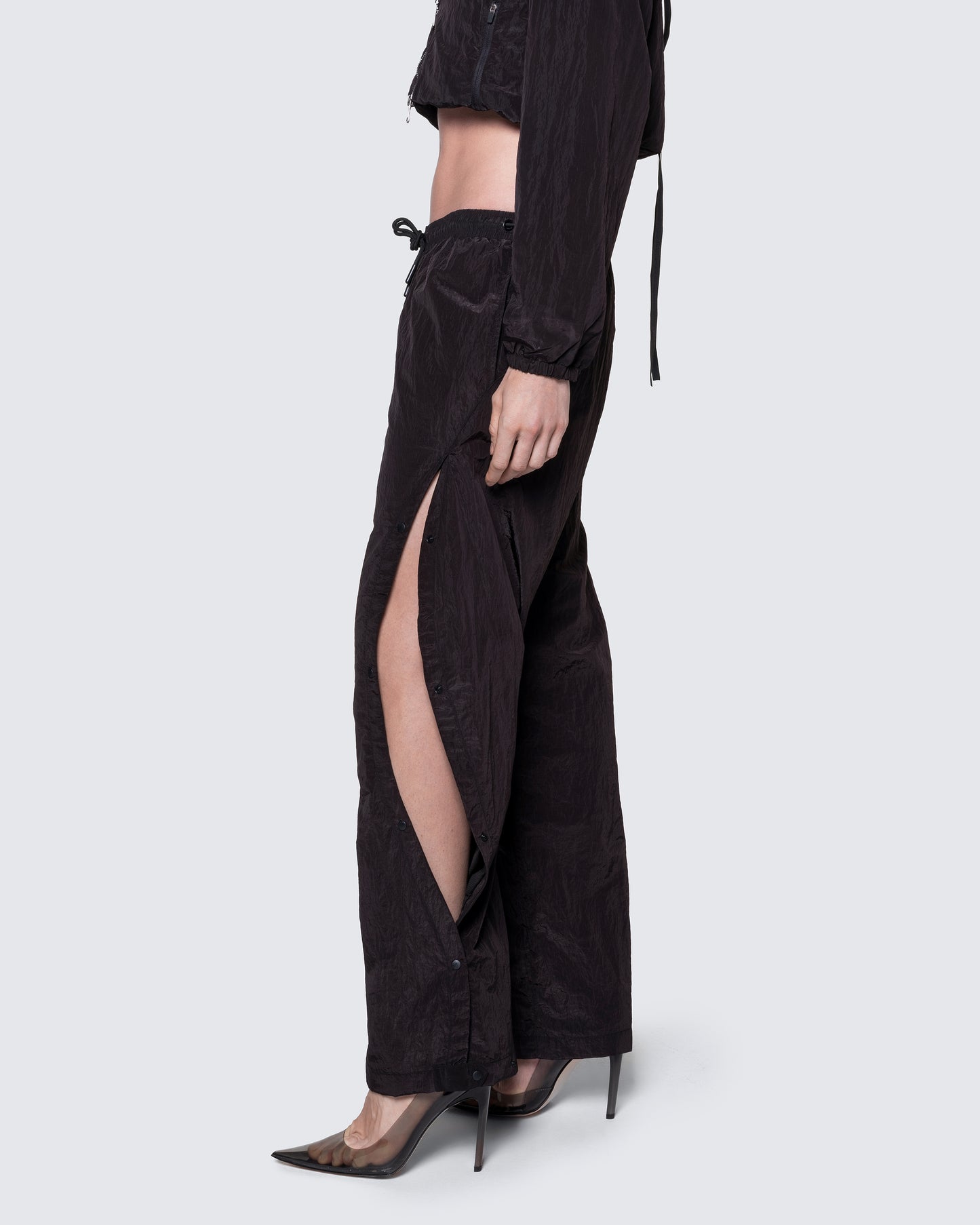 Side view of 12Twelve black track pants featuring curved adjustable slit and lightweight textured fabric
