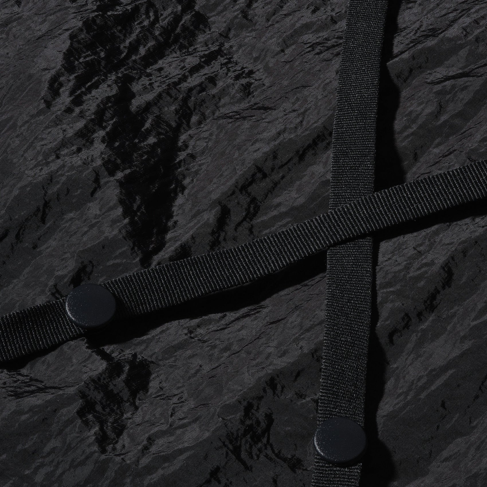 A macro shot of the back of the 12twelve black nylon crop jacket showing the button strap detail. 